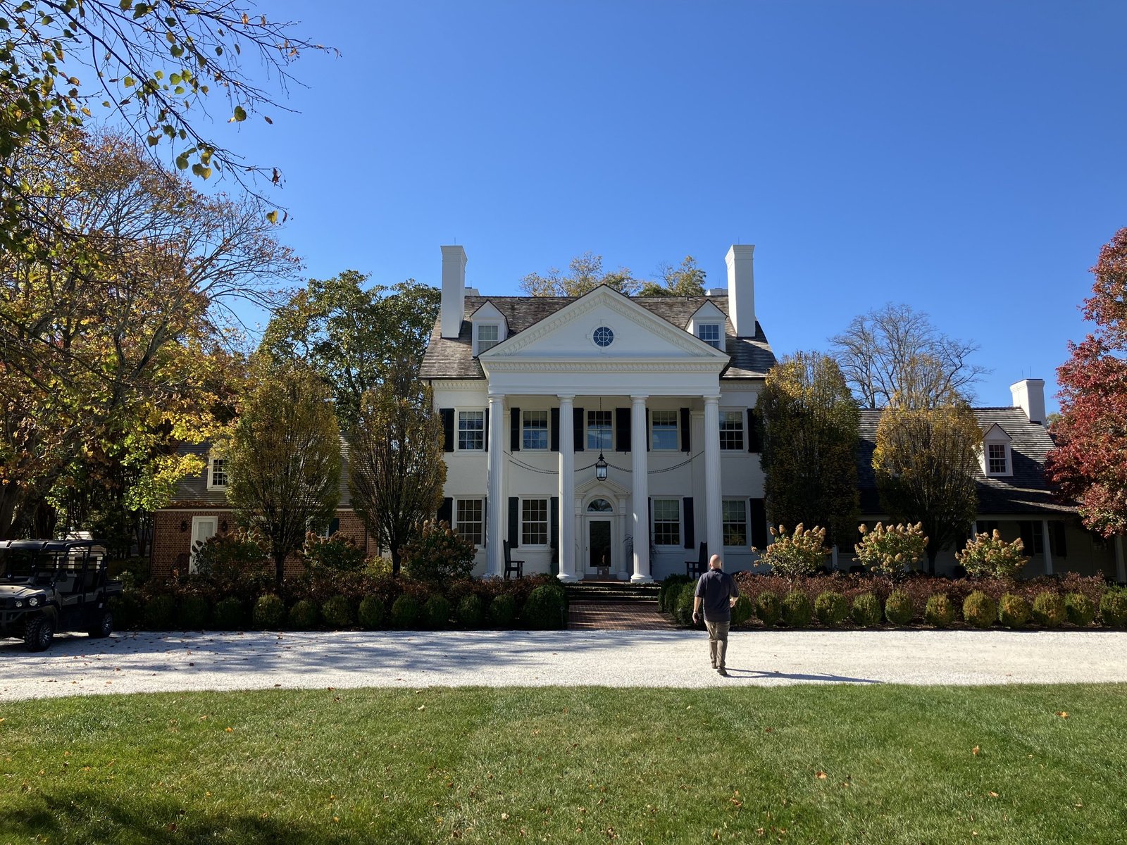 Front elevation of the Georgian Colonial: columned portico, brick wings, gravel drive